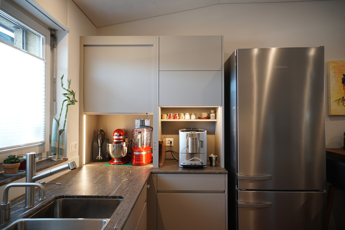 Neue Küchenschränke mit LED-Beleuchtung. Der linke Schrank ist mit einem elektrischen Rolladen in Frontfarbe ausgestattet.